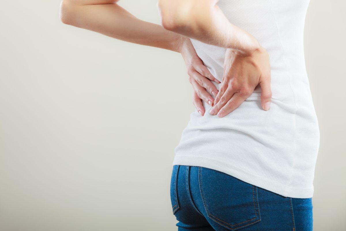 Long working hours and health. Young female with backache. Woman with back pain on gray